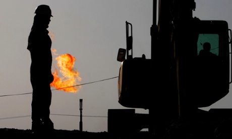 A gas flame burns behind oil field workers in the desert oil fields of Sakhir, Bahrain.