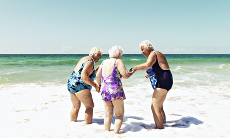 Three old ladies laughing on beach in the surf