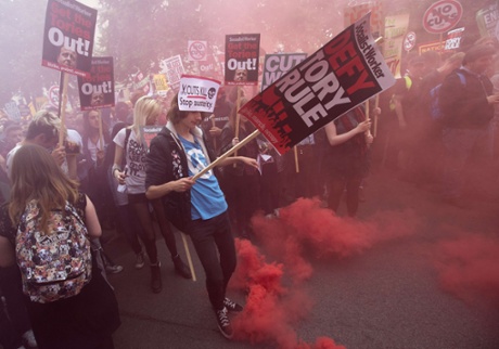 A red flare is kicked by a demonstrator as they march to protest against spending cuts and austerity measures.