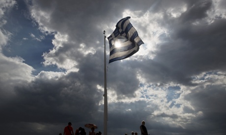 Tourists stand beneath a Greek flag fluttering against  the sun at the ancient Acropolis hill , in Athens, on Monday June 22, 2015