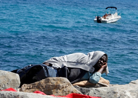 A man relaxes while fishing from his boat while a migrant rests on the seawall at the Saint Ludovic border crossing between Italy and France.