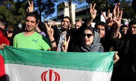 Iranians flash the victory sign as they hold their country's flag while waiting for arrival of foreign minister Mohammad Javad Zarif from Lausanne, Switzerland on 3 April 2015. The lifting of the sanctions has been hailed by Iranians in a recent poll.