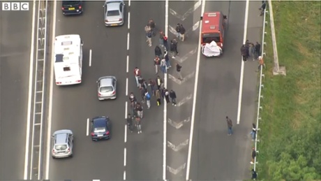 A video grab taken from BBC News of migrants walking among queues of traffic as they search for vehicles they hope might bring them across the Channel