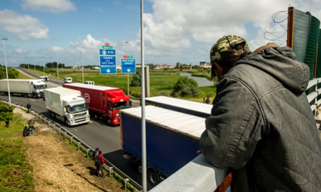 A migrant looks down from a motorway bridge as others wait for lorries they might be able to climb aboard which are heading to Britain