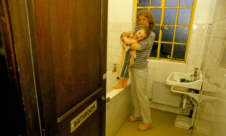 A woman dries her child with a towel in a bathroom at a hostel.
