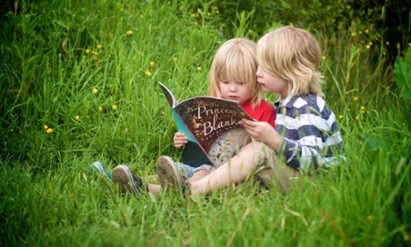 Two young children sitting on grass absorbed in a shared book