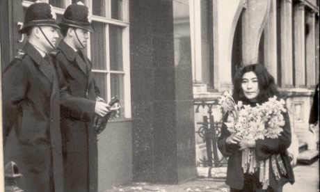 Yoko Ono walking past policemen while carrying daffodils in 1966, after her film ‘No. 4 (Bottoms)’ was banned