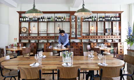 A big table with 10 chairs, hanging lamps and bookshelves behind