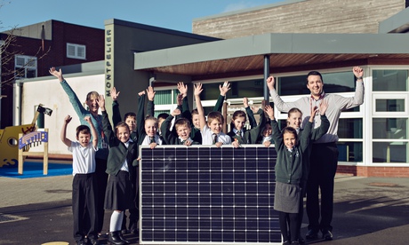 School children and teachers, holding a solar panel, cheer