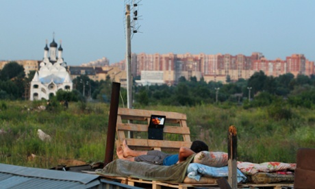 A migrant worker watches a film on his laptop on top of a shelter outside Moscow