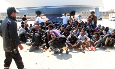 Migrants sit on the ground after being detained by Libyan coast guard