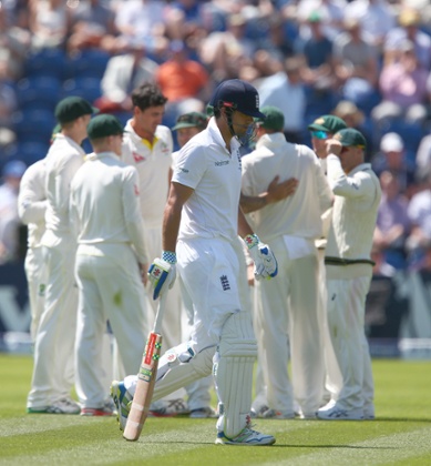 Cook shows a look of dejection as he walks off after being dismissed by Mitchell Starc, who is being congratulated by his team-mates in the background.