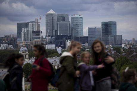 Youngsters take selfies backdropped by the view of the Canary Wharf business district in London, which includes the headquarters building of HSBC, Tuesday, June 9, 2015.