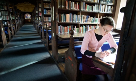 Woman sits at table in library writing notes