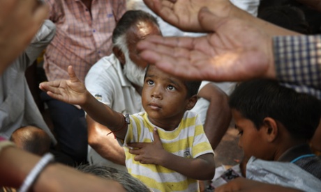 An Indian child stretches arms to receive free food being distributed by a government run program, in New Delhi.