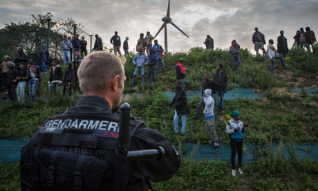 A French police officer faces migrants outside the Eurotunnel terminal