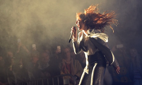 Florence Welch singing at a concert, with her hair flying up, a microphone in her hand