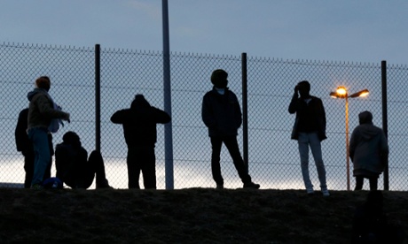 Migrants are seen in silhouette as they stand on a rise near a fence as they gather near the Channel Tunnel access in Frethun, near Calais, France.
