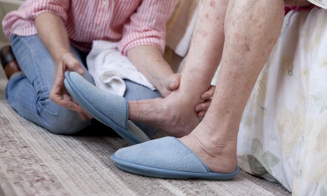 A woman helping an elderly woman put on slippers
