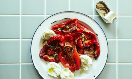 A plate of roasted piedmont peppers on an enamel plate with halved balls of mozzarella, alongside an opened tin of anchovy fillets on a tiled worktop.
