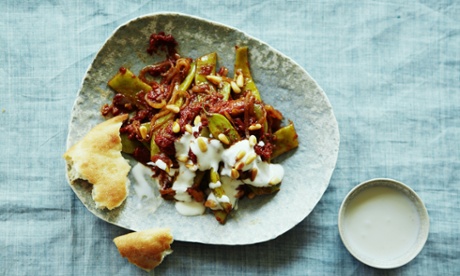 A craft pottery plate on a linen tablecloth, with wilted green beans in a tomato and pepper sauce. Served with pieces of flatbread and sprinkled with plain yoghurt and pine nuts.
