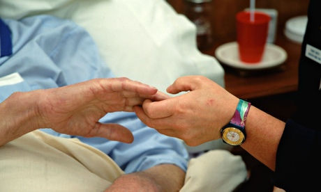 Hospice worker holding the hand of an elderly man.
