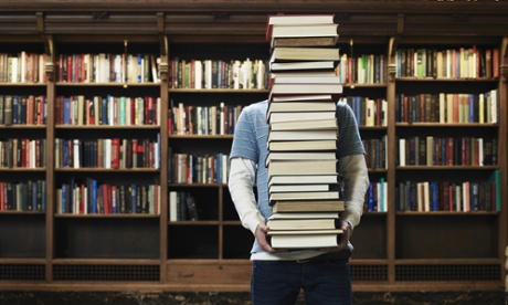 Young man carrying stack of books in a university library.