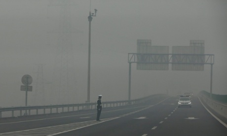 A traffic police officer standing on an expressway is barely visible due to hazardous pollution levels, in Hebei province, China, 26 November 2014.