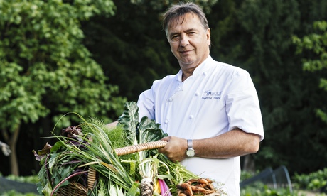 Raymond Blanc, smiling, in a garden holding a flat basket of vegetables