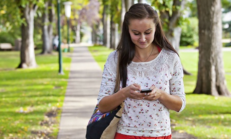 A woman walking through a park smiling and texting