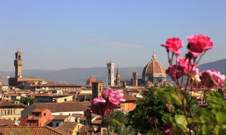 Bright pink roses against a blue sky with the red-tiled roofs of Florence and the cathedral in the background.