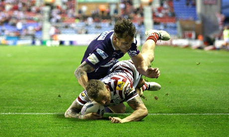 Wigan's Dominic Manfredi scores a try despite an attempted tackle by Scott Grix of Huddersfield 