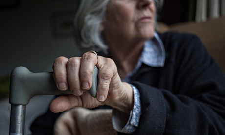 An elderly woman in a care home, her hand on a walking stick