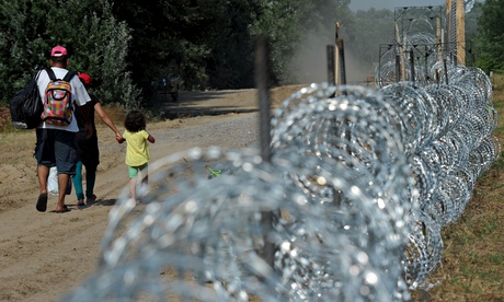 A family walks by a fence that is being built on the Hungarian Serbian border at Morahalom