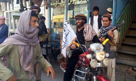 A Taliban fighter sits on his motorcycle adorned with a Taliban flag