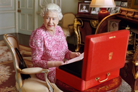 An official photograph of the Queen seated at her bureau with her red briefcase of government letters