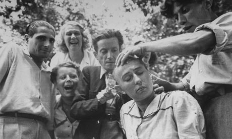 A crowd jeers as a woman's head is shaved during the liberation of