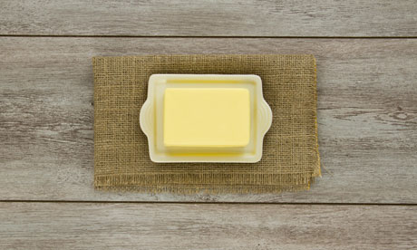 A creamy block of yellow butter on a cream ceramic butter dish on burlap. On weathered boards.