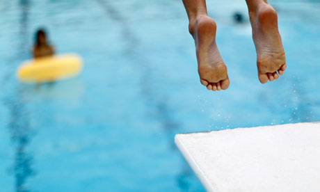 A boy jumps off a diving board into a swimming pool to cool off, in Solana Beach