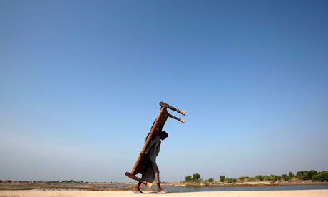 A flood victim carries a bed on his back as he walks to his village in Khairpur district