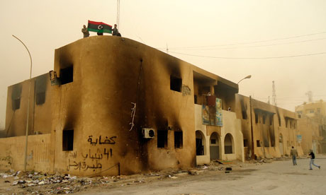 Libyan protesters hold a flag on top of a building.