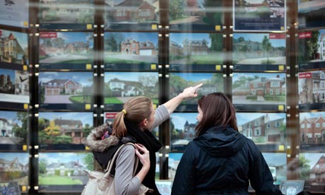 Pedestrians browse residential properties for sale in the window of an estate agent