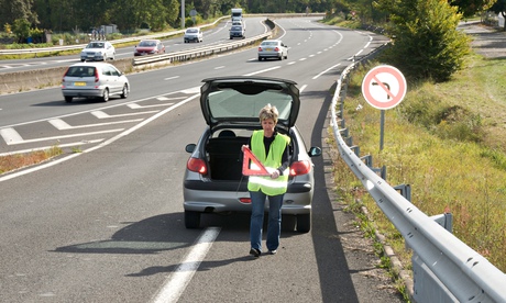 Woman placing warning triangle behind broken down car in France