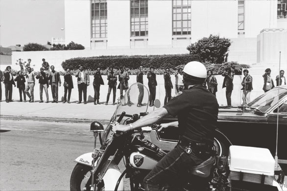 Howard Bingham photos: A row of Black Panthers pretend to shoot at a motorcycle cop