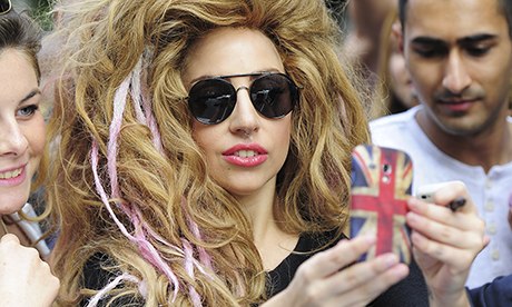 Lady Gaga in a wig holding up a mobile phone to take a picture