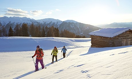 People snowshoeing in South Tyrol in front of trees and hut