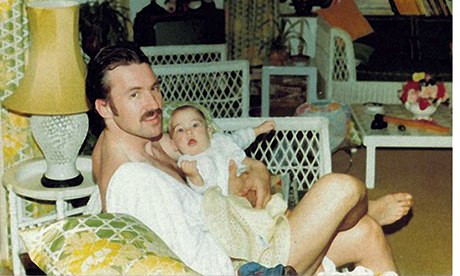 Larry Lamb with a moustache holding baby George in his arms