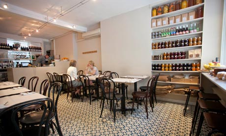 Tables and chairs with shelves of jars at Honey and Co