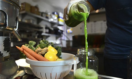 Green juice being poured into a jar next to fresh vegetables