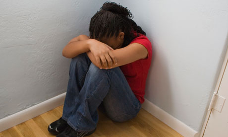 Young woman sitting inthe corner of a room, head in arms